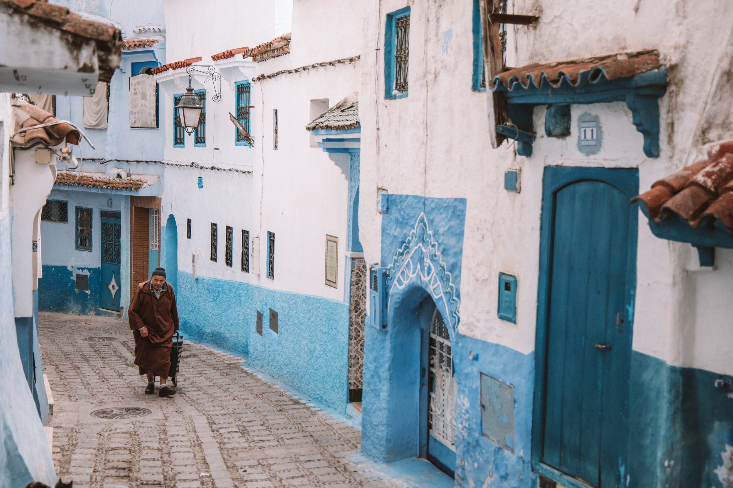 A man in a djellaba walking down a blue-and-white alley in Chefchaouen