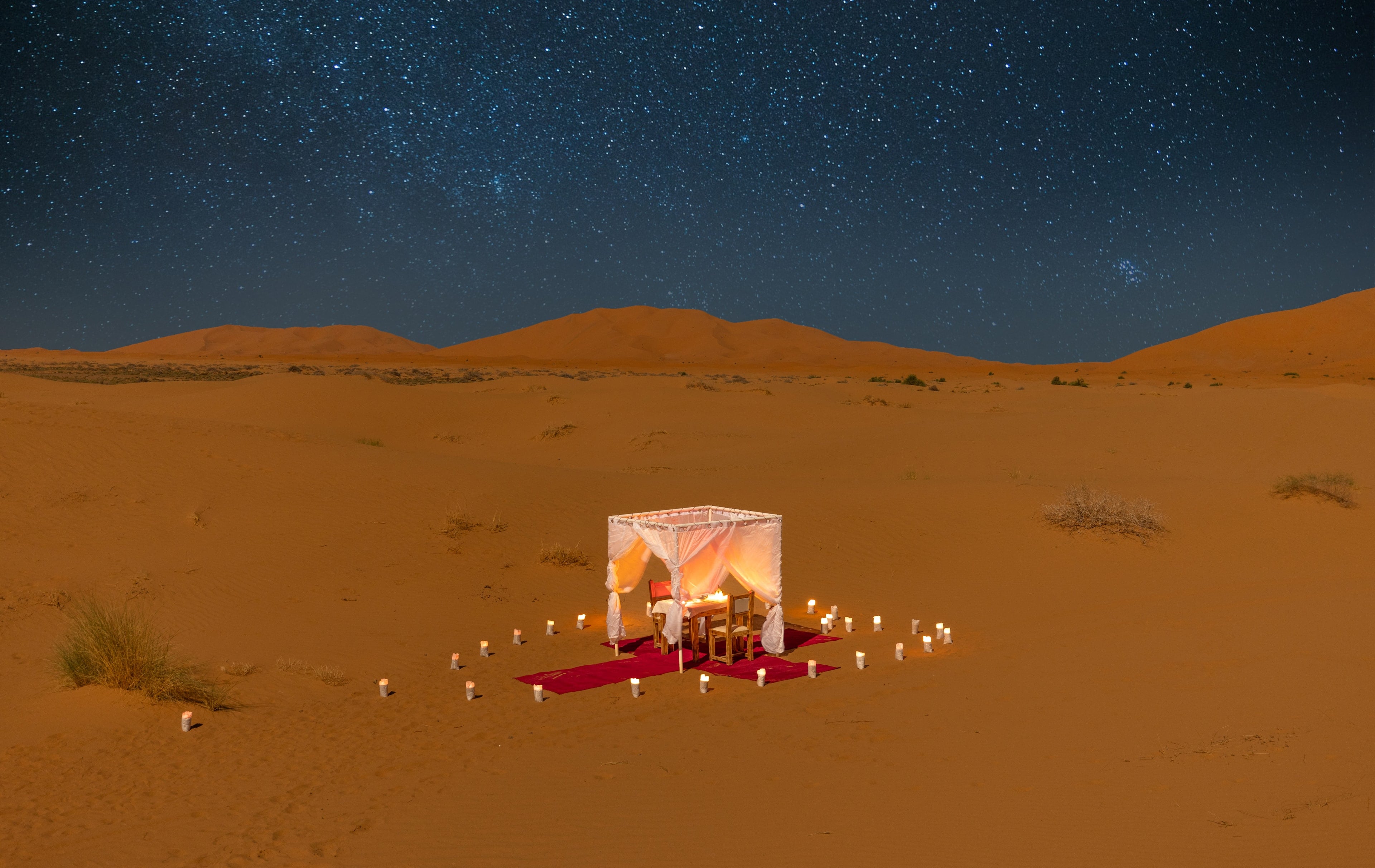A candlelit table for two in the dunes under a starry sky