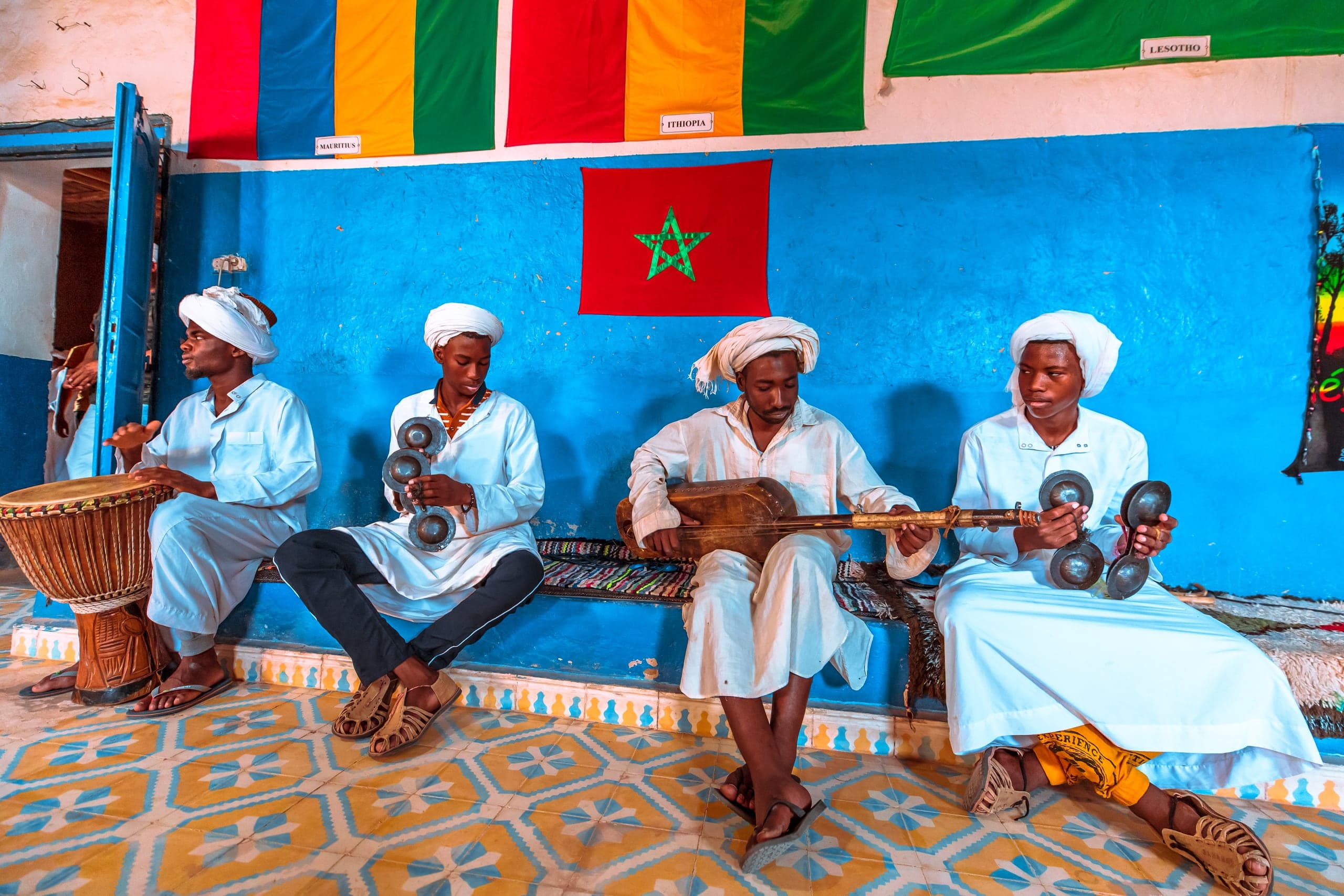 A Gnawa ensemble in white robes playing against a blue wall in Khamlia