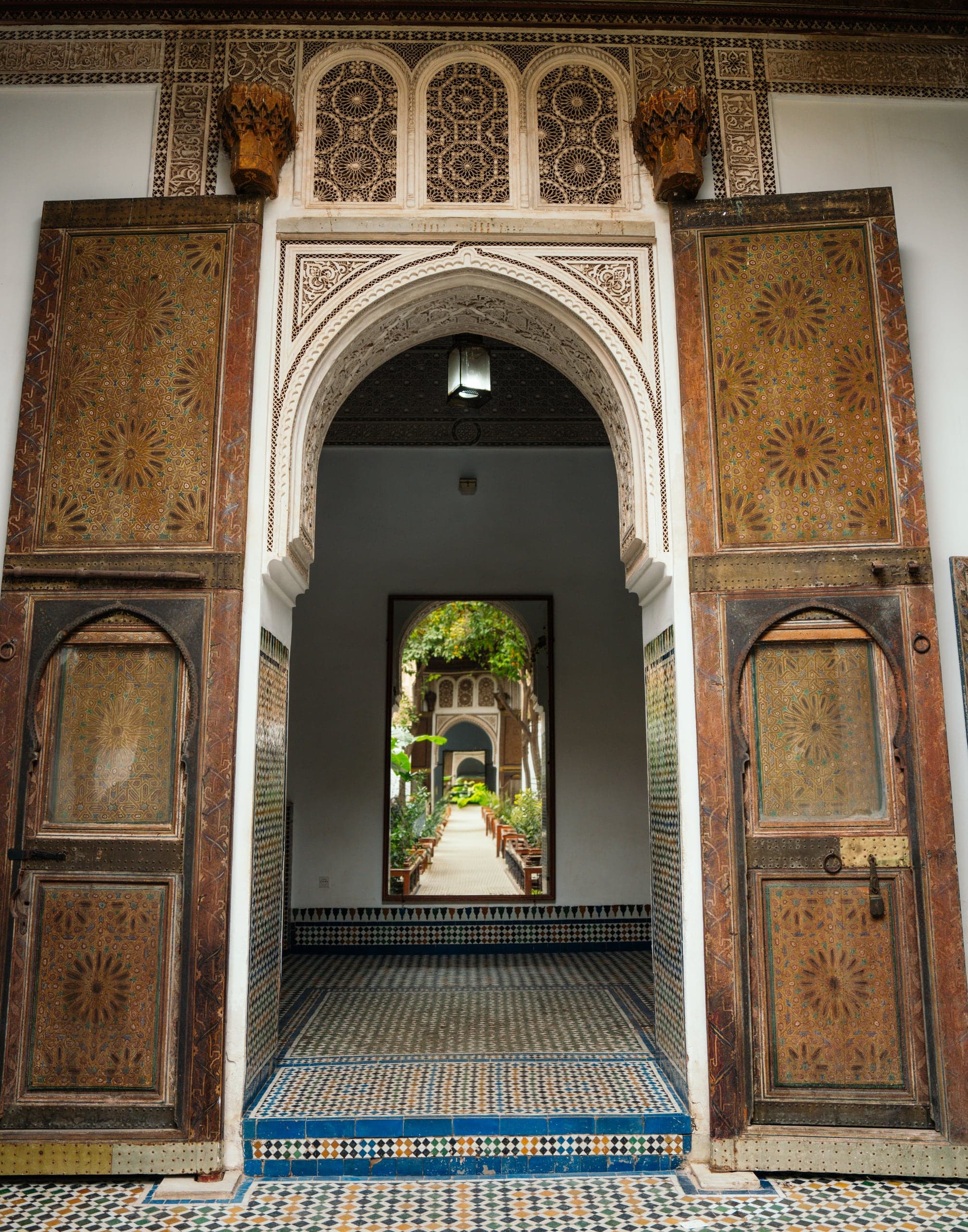 Carved cedar doors opening onto a tiled passage in a Marrakech palace
